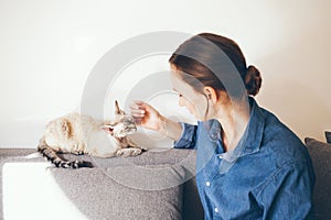 Portrait of a woman in blue jeans shirt is cuddling Devon Rex cat. Cat is feeling happy and relaxed and  purrs. Selective focus