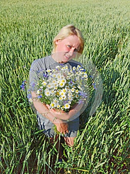 Portrait of woman with bouquet of camomiles and cornflowers in wheat field