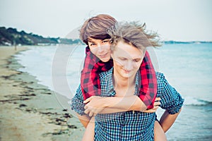 Portrait of woman carrying on happy young man`s back. Couple enjoying each other, having fun on the beach. Date and love story co