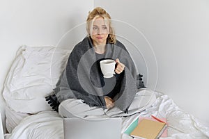 Portrait of woman catching a flu, sneezing, feeling sick, sitting on bed with laptop and working on remote while caught