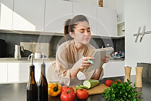 Portrait of woman checking recipe notes in notebook, standing in kitchen with vegetables, cooking food, preparing