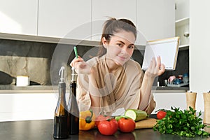 Portrait of woman cooking in the kitchen, reading her notes, checking recipe while preparing meal, making breakfast