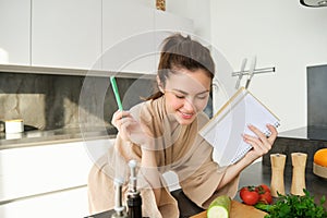 Portrait of woman cooking in the kitchen, reading her notes, checking recipe while preparing meal, making breakfast