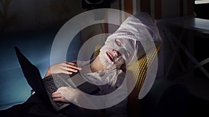 Portrait, woman in cosmetic fabric mask and white towel on her head, fell asleep in front of laptop screen, while