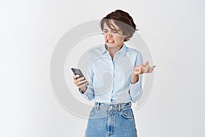 Portrait of woman cringe and look with disgust at mobile screen, reading something disgusting, stare with aversion
