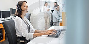 Portrait of woman customer service worker, call center smiling operator with phone headset typing on keyboard at office.