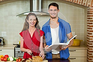 Portrait of woman cutting loaf of bread and man checking recipe book