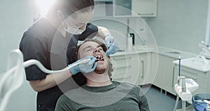 Portrait of a woman dentis and her patient charismatic guy in a dental room have a oral hygiene procedure.
