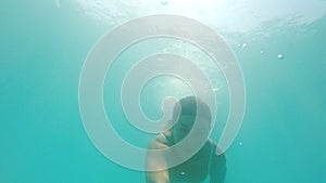 Portrait of woman diving in sea. Girl swimming under water and filming himself with sun flare at background. Female