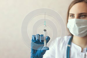 Portrait of woman doctor with a syringe,  on background in blue gloves