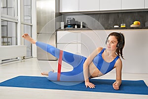 Portrait of woman doing fitness exercises at home, stretching resistance band with legs, focusing on workout training
