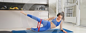 Portrait of woman doing fitness exercises at home, stretching resistance band with legs, focusing on workout training