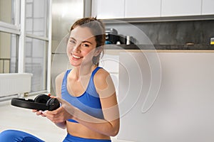 Portrait of woman doing home fitness exercises on yoga mat, listening music in wireless headphones, focusing on workout