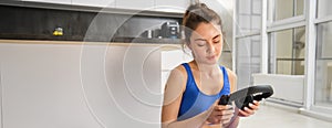 Portrait of woman doing home fitness exercises on yoga mat, listening music in wireless headphones, focusing on workout