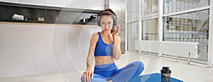 Portrait of woman doing home fitness exercises on yoga mat, listening music in wireless headphones, focusing on workout