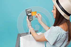 Portrait woman in dress, hat holding packages bags with purchases after shopping, wireless modern bank payment terminal