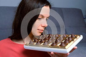 Portrait of woman is eating chocolate candies from box smelling them before it.