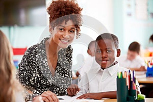 Portrait Of Woman Elementary School Teacher Giving Male Pupil Wearing Uniform One To One Support