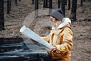 Portrait of woman enjoy travel in the nature forest woods with car - female people look the map on the nose of the vehicle lost in