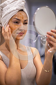 Portrait woman enjoying domestic beauty care procedure with peeling scrub mask on face mirror