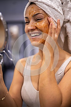 Portrait woman enjoying domestic beauty care procedure with peeling scrub mask on face mirror