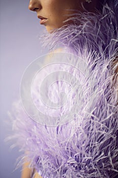 portrait woman in an evening purple dress with feathers stands in the background in the studio.