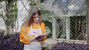 portrait of woman farmer writing notes in notepad in greenhouse, modern agribusiness and farming