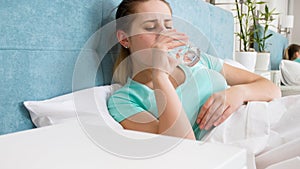 Portrait of woman feeling unwell lying in bed and drinking water