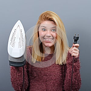 Portrait of woman with funny face holding iron against gray background