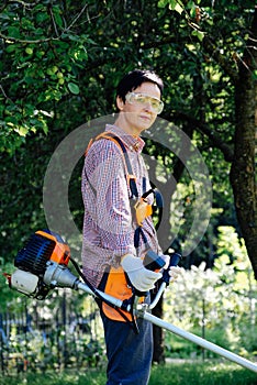 Portrait of woman gardener mowing the grass on backyard using string trimmer