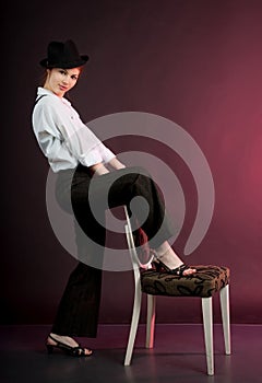 Portrait of woman, girl in man\'s suit with suspenders and hat stands with chair