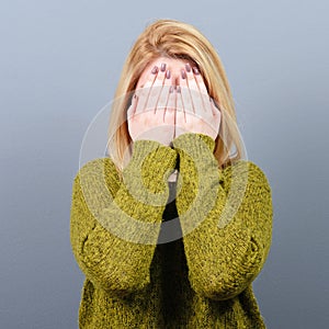 Portrait of woman hiding her face with both hands against gray background