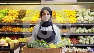 Portrait of a woman in hijab standing with basket of fresh vegetables in the supermarket