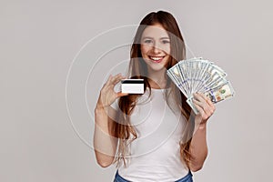 Portrait of woman holding credit card and big fan of dollar banknotes, banking, earning money.