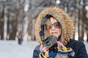 Portrait of a woman holding a digital camera in the woods in win