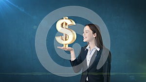 Portrait of woman holding golden dollar sign on the open hand palm, over isolated studio background. Business concept.