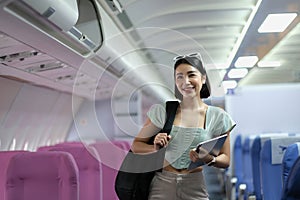 Portrait of a woman holding a shoulder bag and holding a tablet while standing on a passenger plane