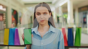 Portrait woman holding smartphone , showing green screen phone to camera in the mall. Chroma key smartphone.Green screen