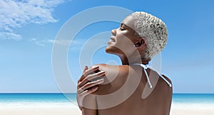 Portrait of a woman on the hot summer beach, enjoying a holiday by the sea. Seen from behind, with her hand on her shoulder,