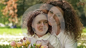 Portrait of a woman hugging her teenage daughter with a bouquet of tulips. Against the background of spring nature
