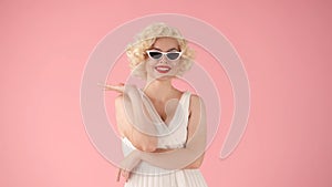 Portrait of a woman in the image of Marilyn Monroe wearing cat eye shape sunglasses in studio on pink background.