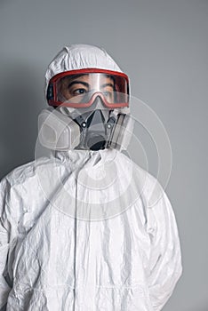 Portrait of woman in lab coat, nitrile gloves, goggles, face mask and NBC protective suit with gray background