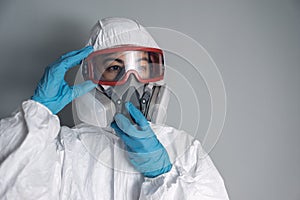 Portrait of woman in lab coat, nitrile gloves, goggles, face mask and NBC protective suit, putting on equipment