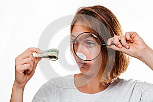 Portrait of a woman looks through a magnifying glass at a small wad of dollars. White background. The concept of checking