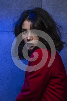 Portrait of woman with makeup and hairstyle, wear red suit, looking at camera, blue neon studio light.