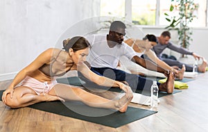 Portrait of woman making stretching legs with multinational group sitting on sports mat and making yoga exercise at