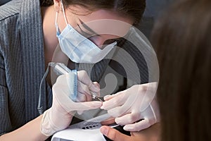 Portrait of woman manicurist in mask cleaning pterygium on nail using apparatus. photo