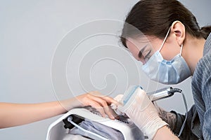 Portrait of woman manicurist in mask cleaning pterygium on nail using apparatus. photo