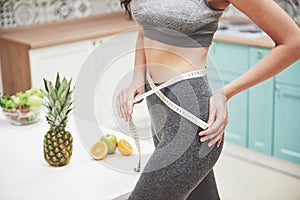 Portrait of a woman measuring her slim body on a kitchen background. Fitness and healthy lifestyle concept