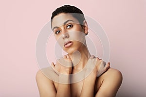 Young woman naked shoulders clean skin and nude make up posing over pink wall in front of a camera. Space for text. photo